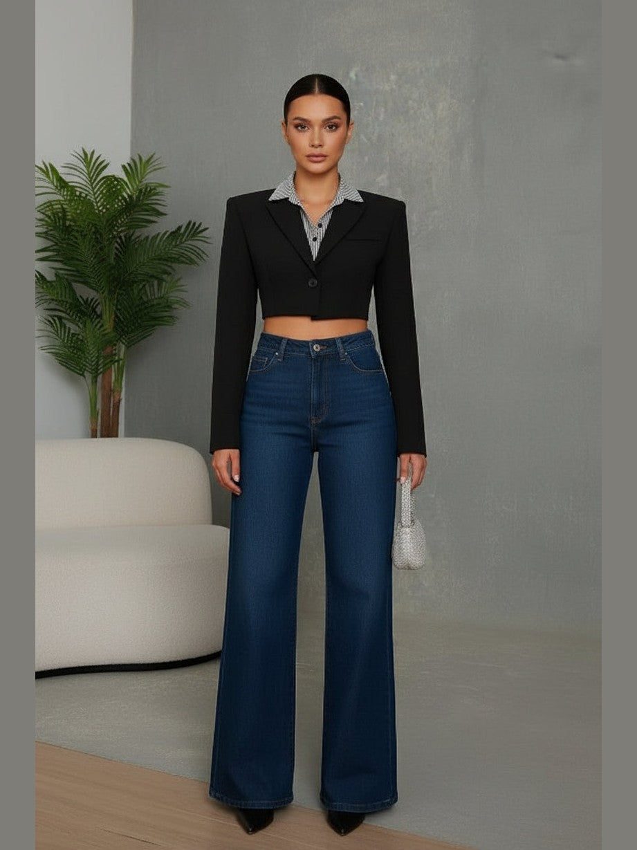 Person wearing a black cropped jacket and blue jeans against a gray background