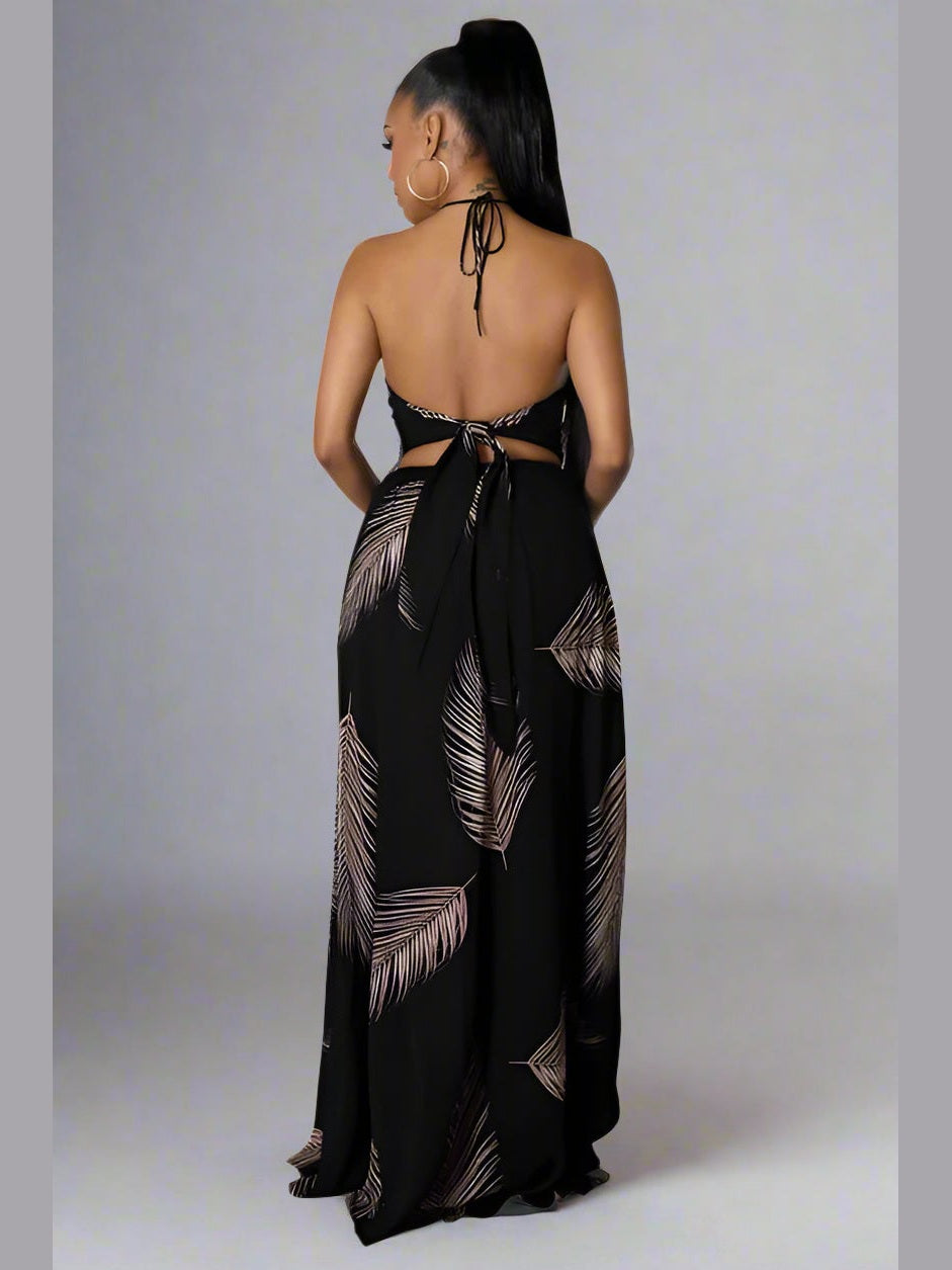 Black halter neck maxi dress with deep V-neckline, sleeveless cut, open back with a self-tie, elastic waistband, and a flowy, draped skirt. Model facing backward.