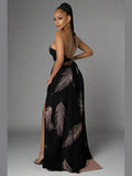 Black halter neck maxi dress with deep V-neckline, sleeveless cut, open back with a self-tie, elastic waistband, and a flowy, draped skirt. model standing to the side.