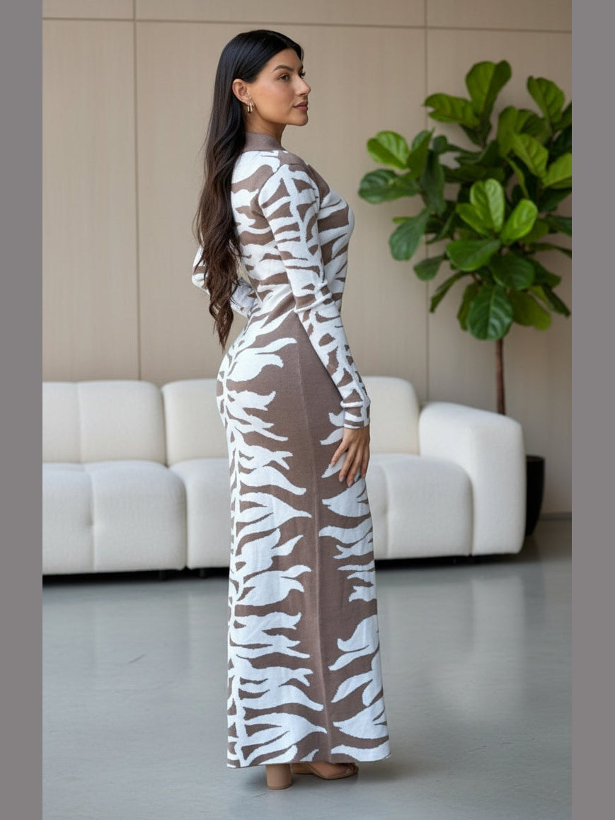 Woman wearing a long, patterned dress standing against a building wall.