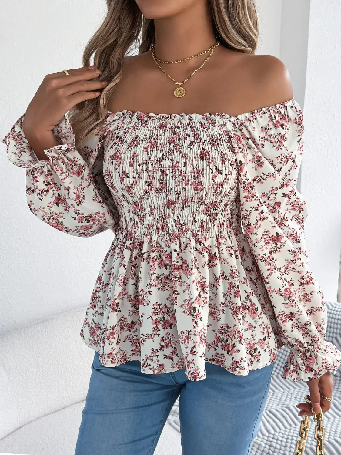 Off-shoulder floral blouse with a vibrant floral pattern, elastic neckline, and flowy sleeves, perfect for a feminine and effortless look in white. Model has hand on her shoulder