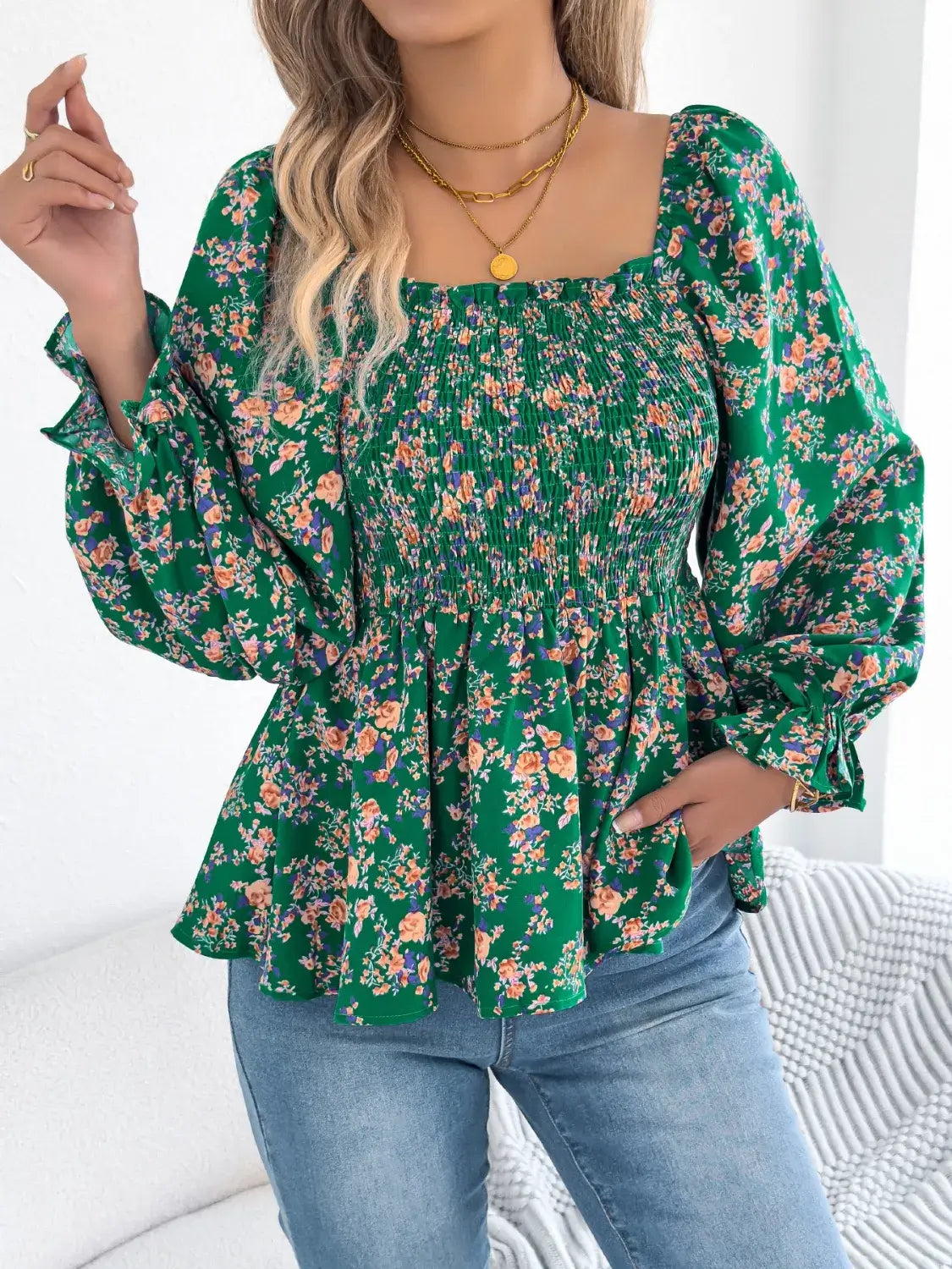 Off-shoulder floral blouse with a vibrant floral pattern, elastic neckline, and flowy sleeves, perfect for a feminine and effortless look in green with model right hand lifted
