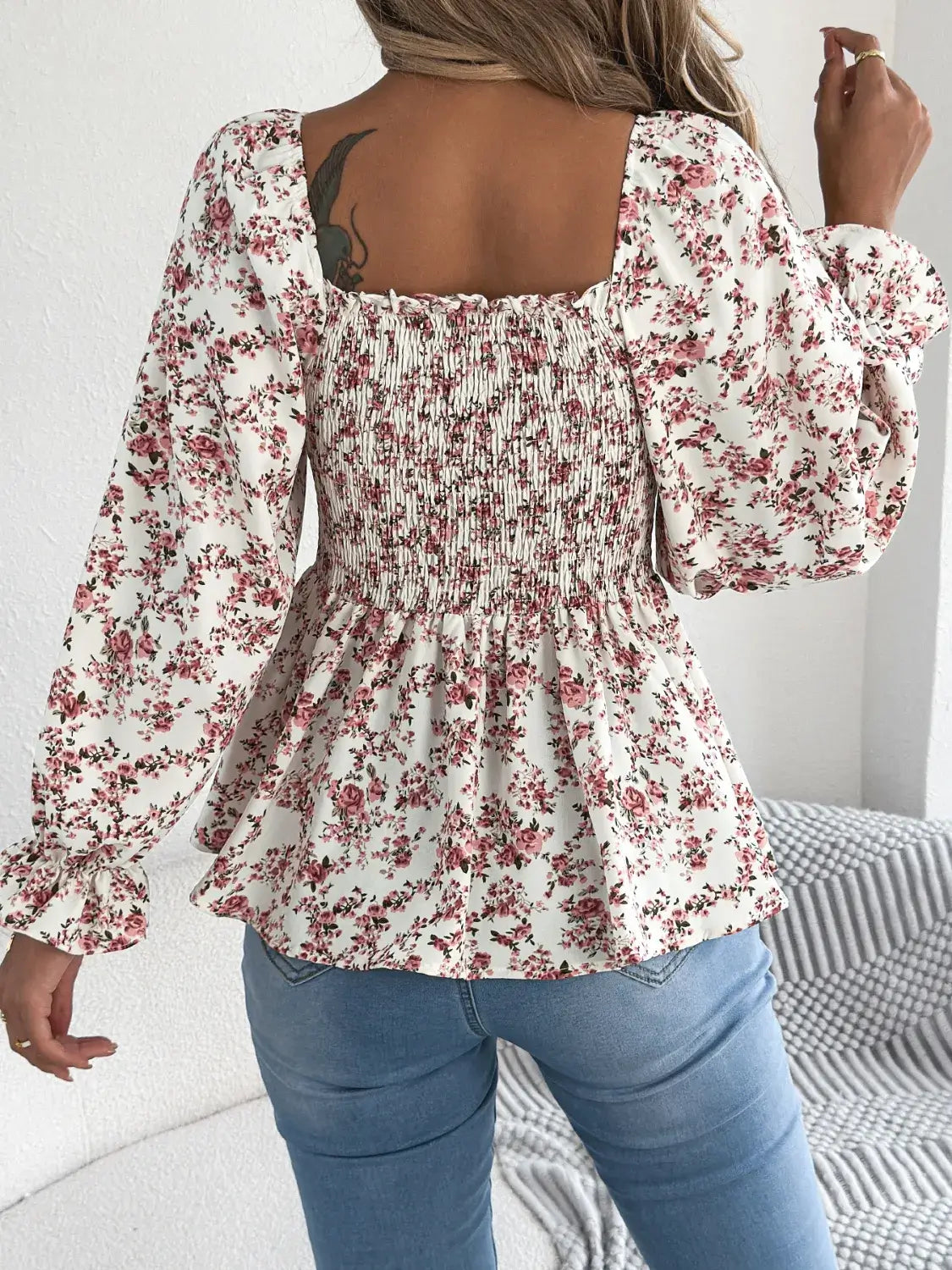 Off-shoulder floral blouse with a vibrant floral pattern, elastic neckline, and flowy sleeves, perfect for a feminine and effortless look in white facing backwards