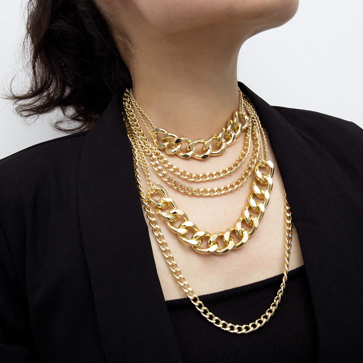Person wearing multiple gold chain necklaces on a plain background