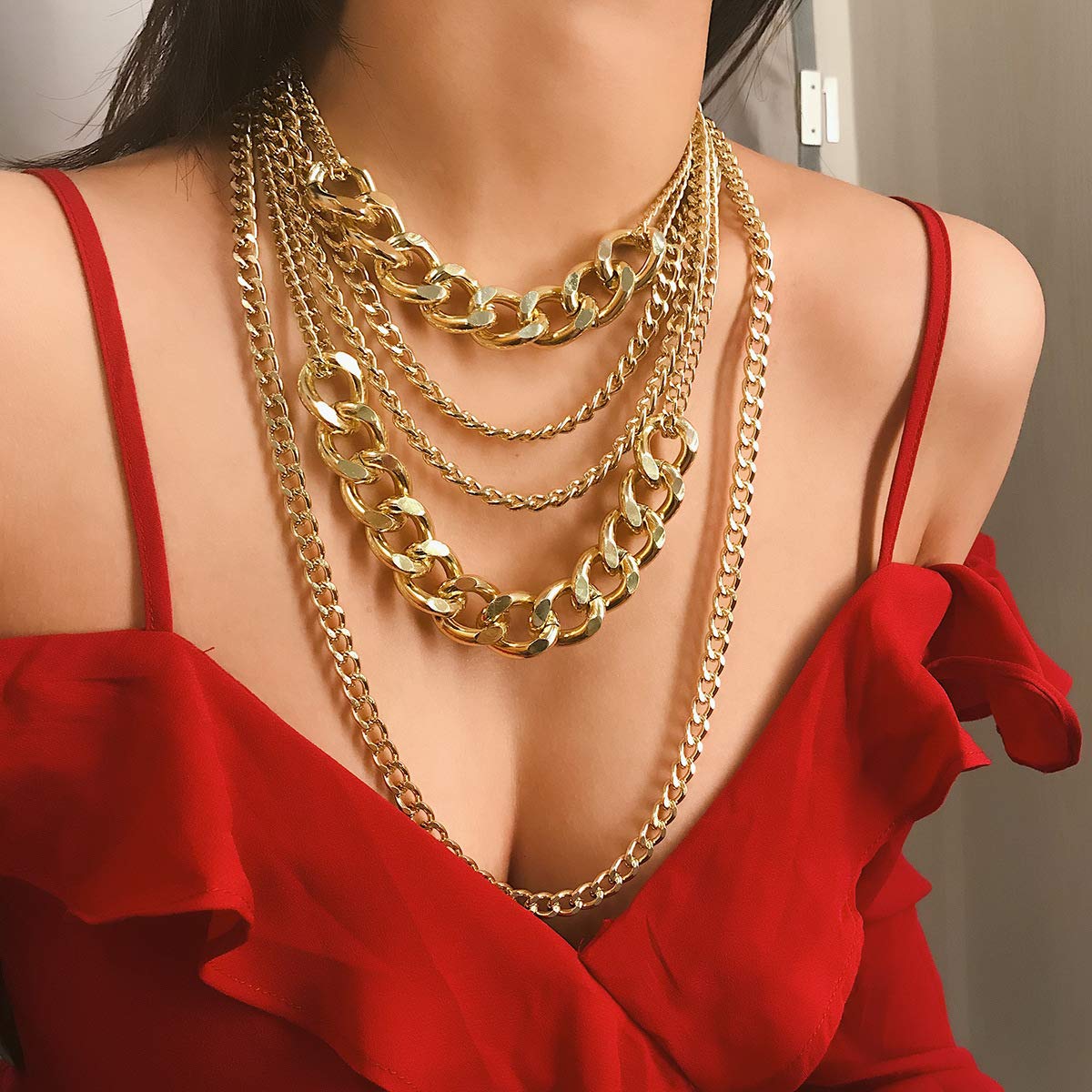 Woman wearing a red top and multiple gold chain necklaces.