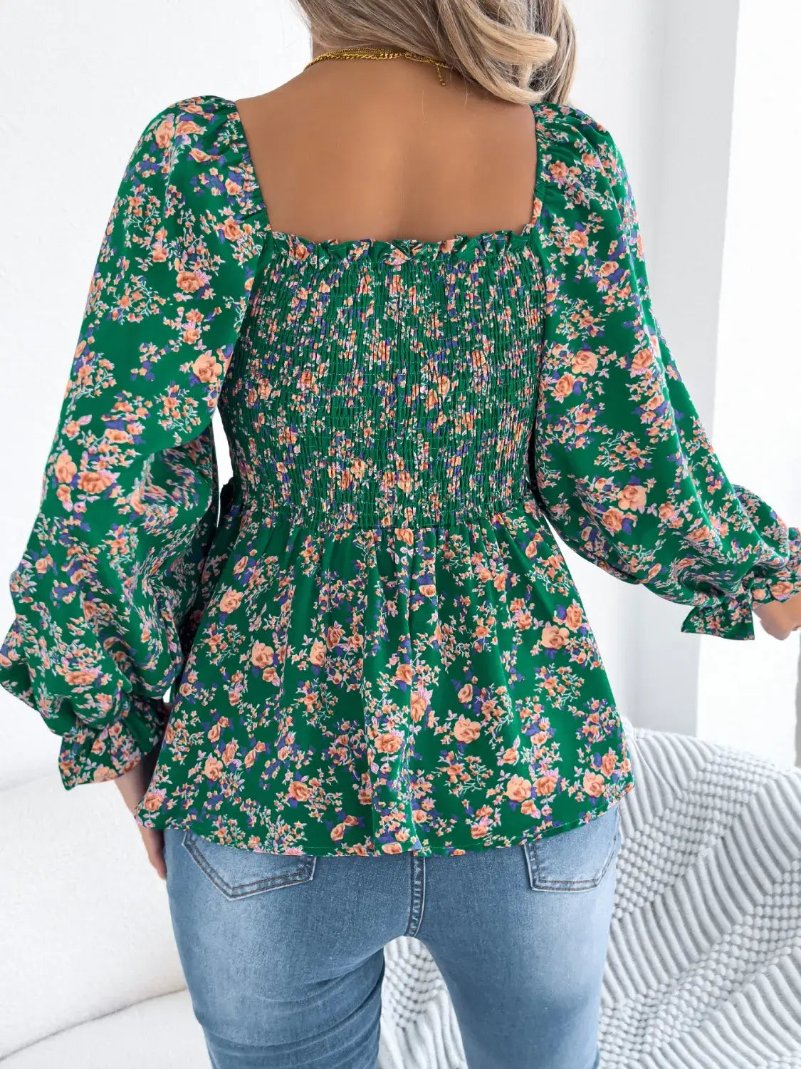 Off-shoulder floral blouse with a vibrant floral pattern, elastic neckline, and flowy sleeves, perfect for a feminine and effortless look in green facing backward

